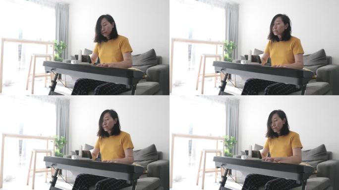 亚洲成年母亲在家中靠窗的沙发上通过手机应用程序学习键盘乐器，生活方式理念。
