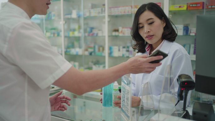亚洲男子顾客扫描付款二维码在药店购买药品。