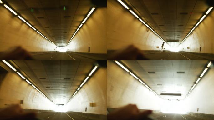 一名白人男子把手放在方向盘上，驾车穿过一条隧道，在明亮的灯光下离开