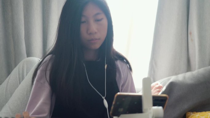 亚洲女孩在家里玩手机游戏的哥哥旁边的沙发上通过手机应用程序学习键盘乐器，生活方式理念。