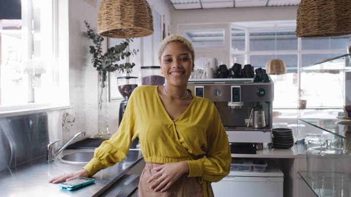 快乐的年轻千禧一代非洲裔美国女企业家在当代厨房摆出造型。 一个年轻的黑人创业女孩站在咖啡店，微笑着看