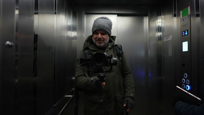 Vlogger男子在电梯中使用万向架相机，镜子自拍肖像