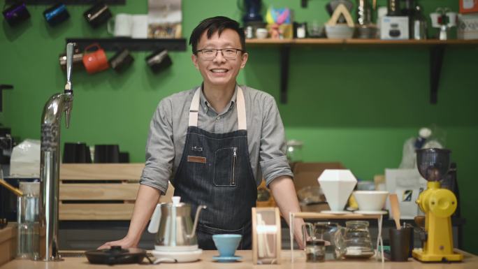 咖啡馆柜台上的亚洲中国咖啡师微笑着看着镜头