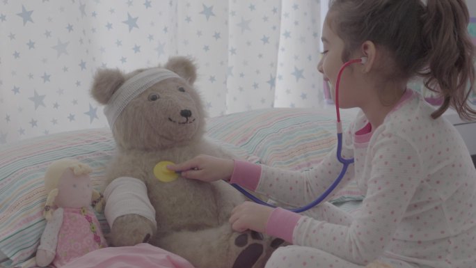 小女孩在床上和泰迪熊玩医生