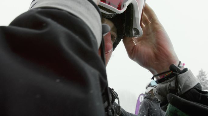 慢镜头拍摄的是一名20多岁的男性滑雪运动员戴上护目镜，准备在雪地上滑雪。冬日