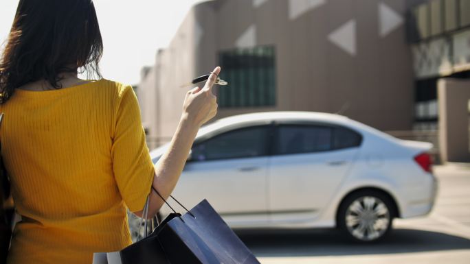购物日后，亚洲妇女背着购物袋和钥匙链走回汽车的后视图