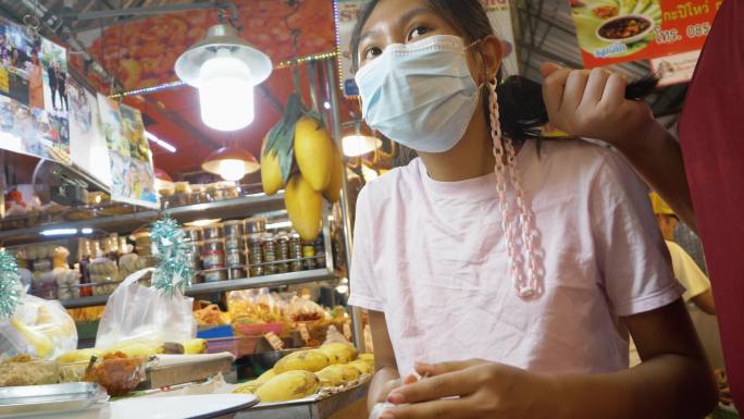 在泰国著名的海鲜市场华欣夜市，亚洲儿童戴着口罩，买芒果糯米饭。