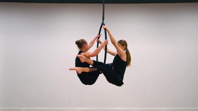 两名空中杂技演员在空中抱箍上表演，展示成对对称的身体形状