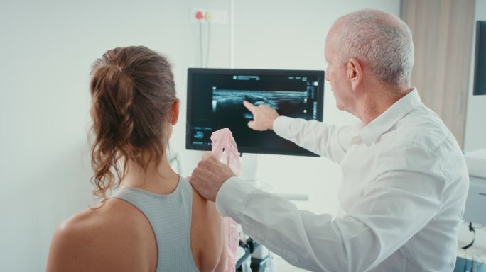 成熟的物理治疗师使用超声波扫描检查患者的肩部损伤。医学运动科学家指出、展示、谈论和解释过度训练导致的