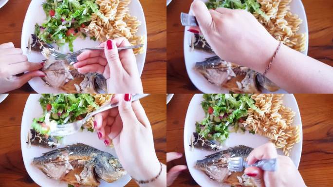 4k视频全炸鱼配上一片柠檬、番茄和芝麻菜沙拉叶，装在白色盘子里。女人在吃鱼，叉子和刀子插在里面，盘子
