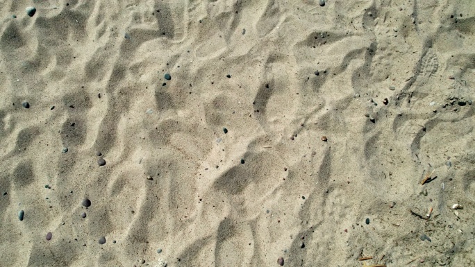 沙滩上的沙子带有鹅卵石、贝壳、细枝和其他碎屑。可见的香烟残留物和足迹。完美的背景。版本3。