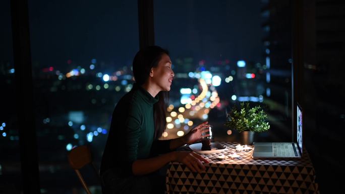 一位亚洲华裔美女在神奇的黄昏时分在公寓里吃甜点，并用笔记本电脑上网与男友聊天