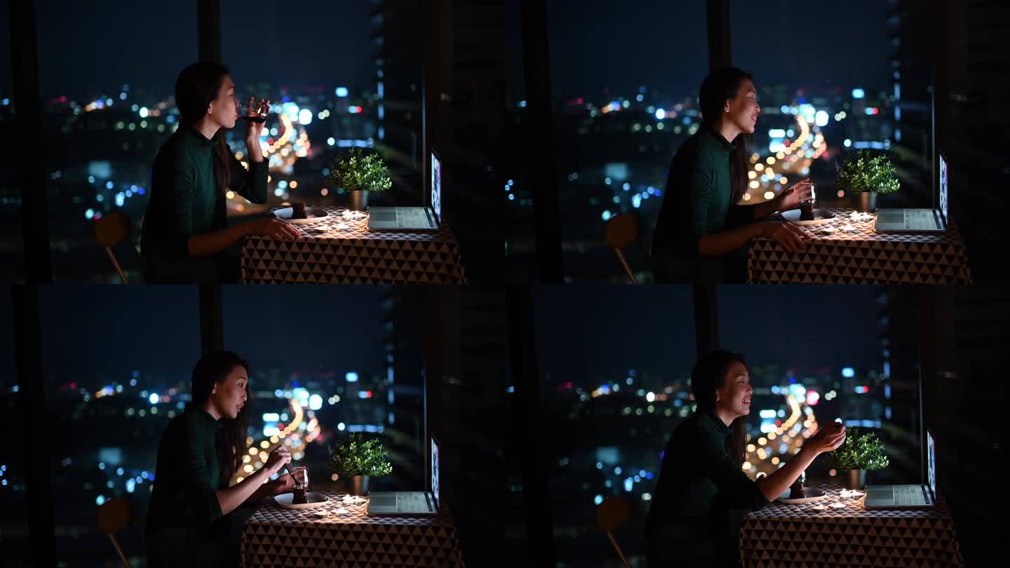 一位亚洲华裔美女在神奇的黄昏时分在公寓里吃甜点，并用笔记本电脑上网与男友聊天