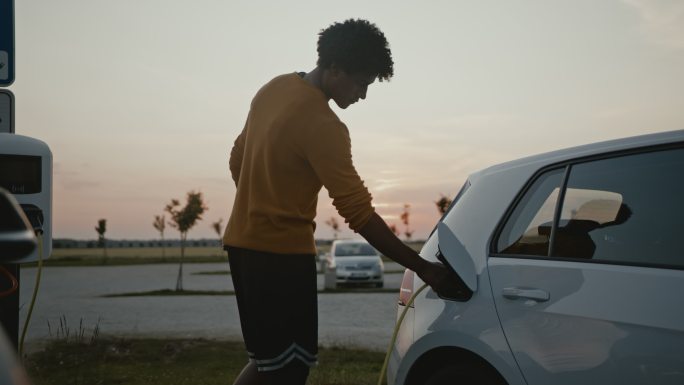 SLO MO年轻的篮球运动员在黄昏时在停车场给自己的电动车充电时，一边打篮球