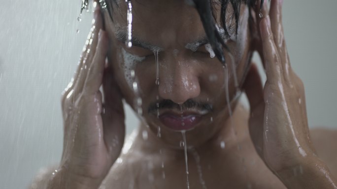 一个年轻人在浴室淋浴下洗黑发的特写镜头