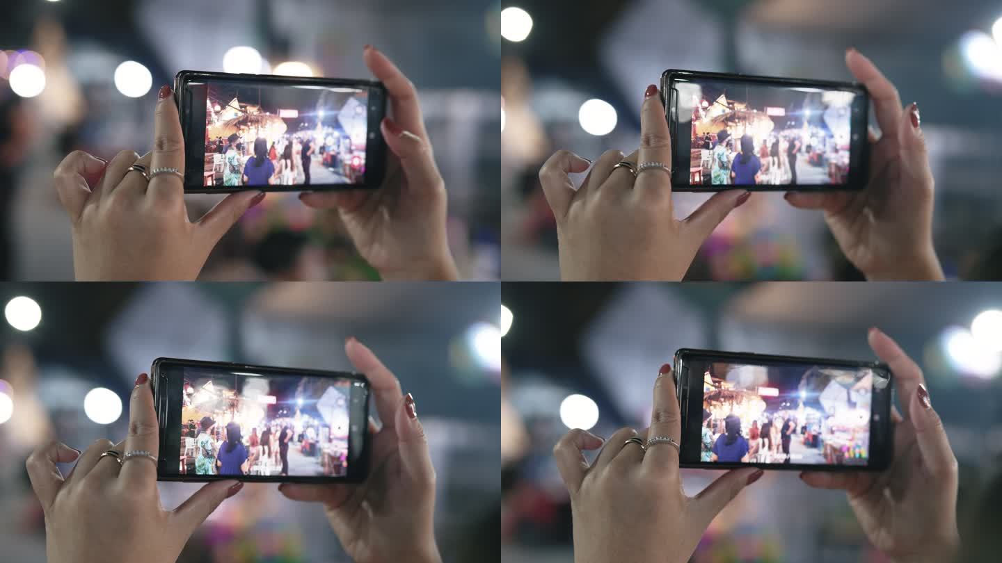 亚洲年轻女子用手机拍摄街头食品市场。
