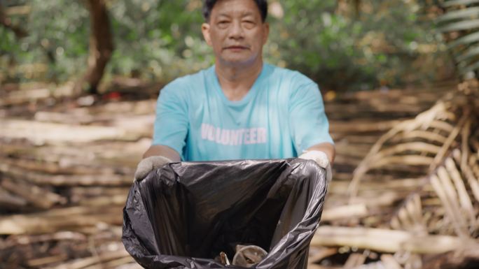 亚洲老年人志愿者自豪地展示了他在红树林中收集垃圾袋和塑料袋，以拯救地球，积极的老年人，可持续的生活方