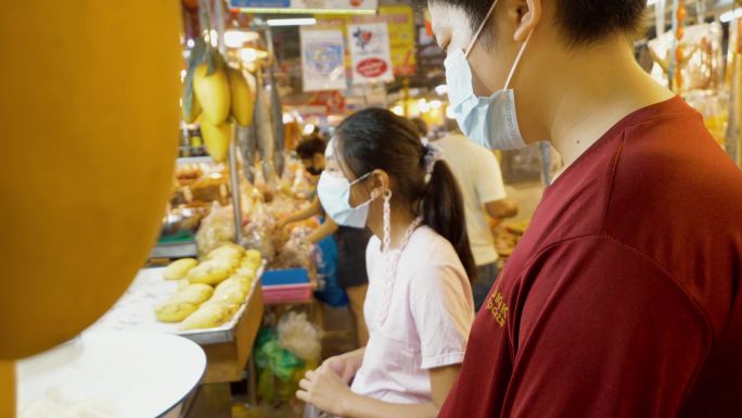 在泰国著名的海鲜市场华欣夜市，亚洲儿童戴着口罩和芒果糯米。