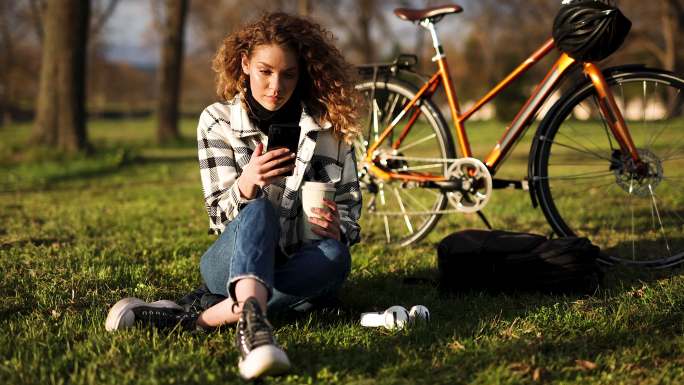 年轻的女自行车运动员在春季日落时使用手机