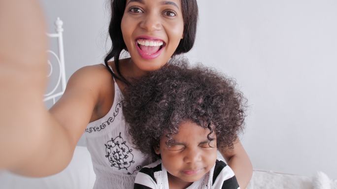 快乐的非洲母亲和儿子给父亲或亲戚拍自拍或视频电话，社交疏远以防止冠状病毒或19型冠状病毒的流行。技术
