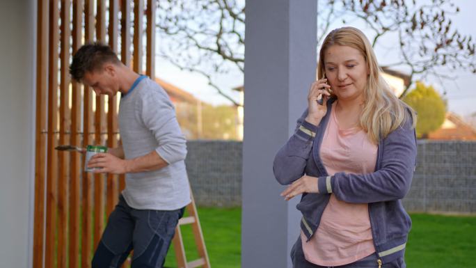 女人在手机上讲话，而男人在背景上画木架