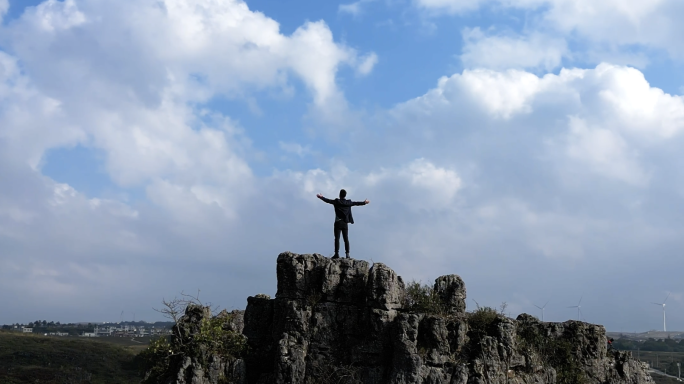 男人山顶张开双臂拥抱天空蓝天白云登山成功