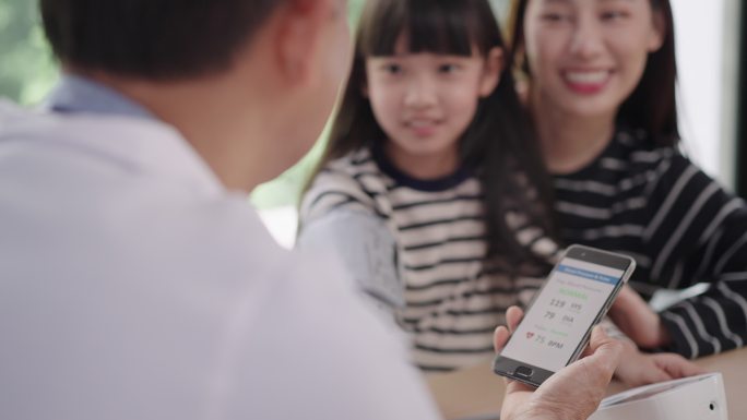 在智能手机界面应用程序中，年轻的亚洲男性护理者、医生坐在医院为年轻母亲的十几岁女孩患者检查血压和心跳