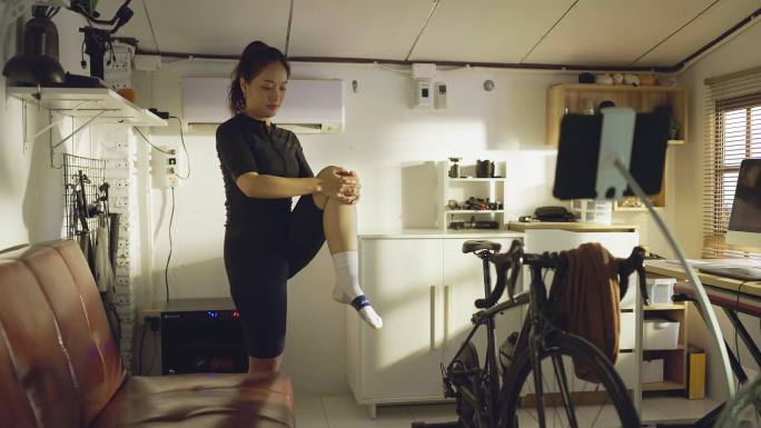 亚洲女自行车运动员，她在家锻炼。她骑自行车模拟器。她伸懒腰