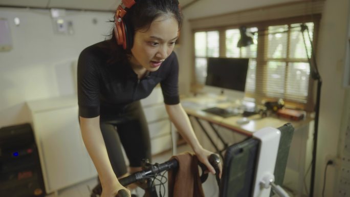 亚洲女自行车运动员，她在家锻炼。她骑自行车模拟器。