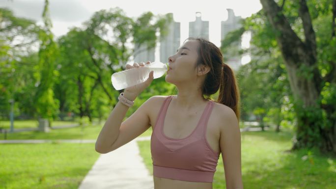 一位在公园锻炼的亚洲女性正在喝水解渴。