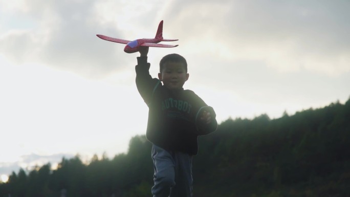 小孩拿着飞机模型草地逆光奔跑孩子微笑脸庞