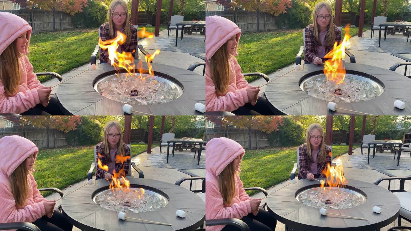 两个年轻女孩在后院的火坑周围烤棉花糖