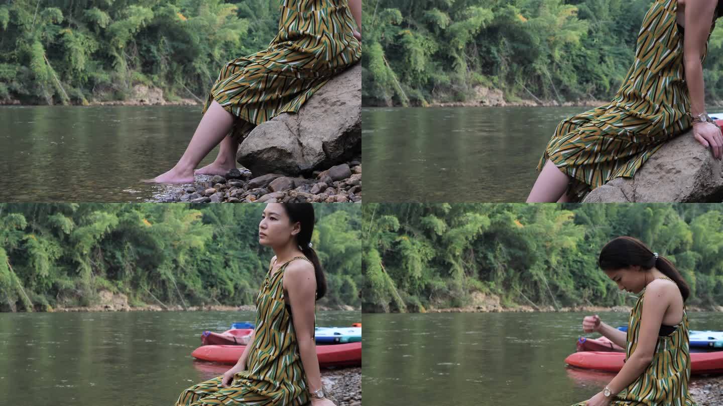 女子坐在岩石上，在湖边放松，双脚在水面附近摆动