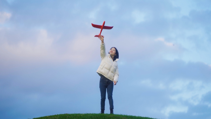 女生站在山顶扔飞机模型放飞梦想和希望意境