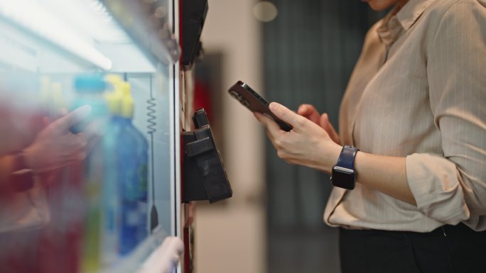 亚洲女性用智能手机向自动售货机付款