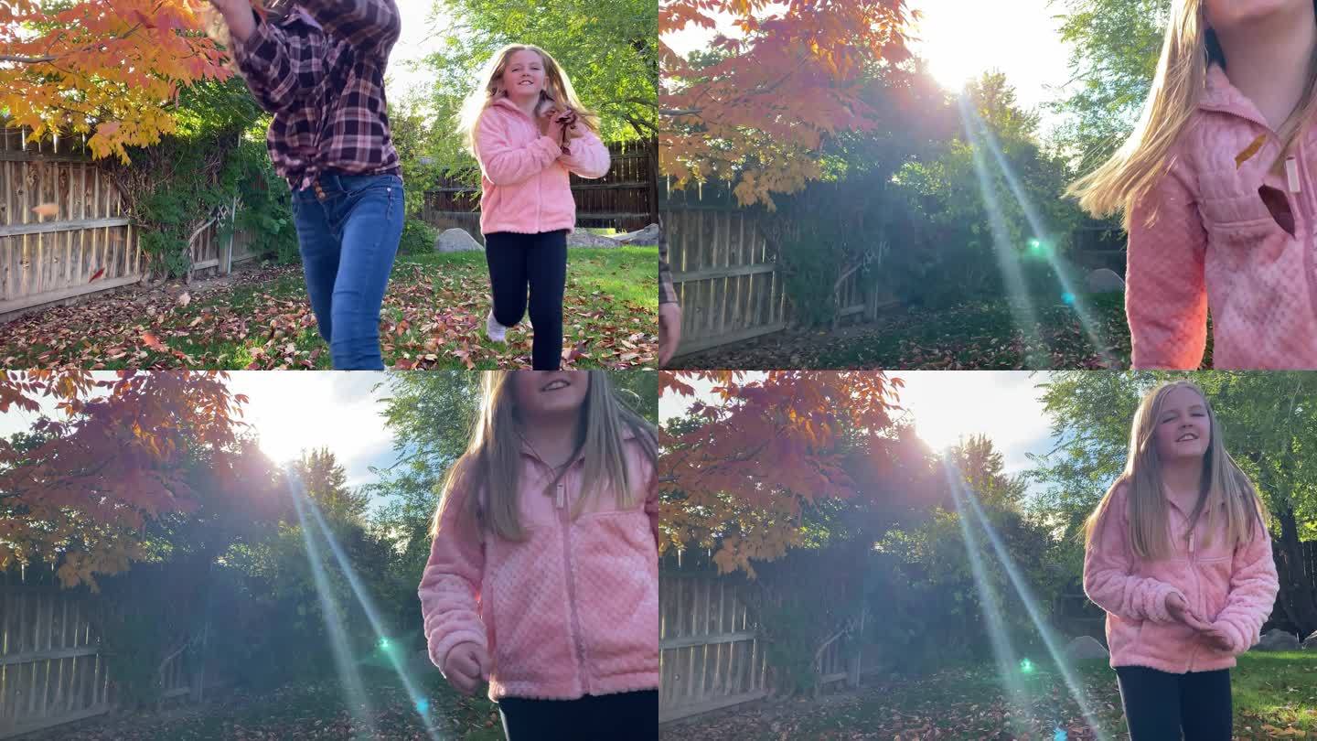 两个年轻的女孩跑过绿色的后院，手里拿着一把秋天的树叶笑着，她们把树叶扔到镜头前，继续笑着