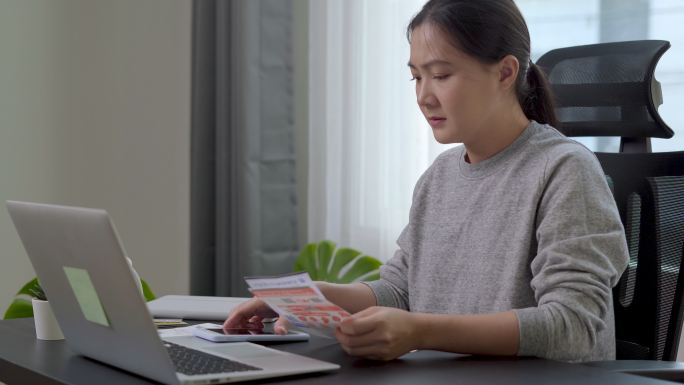 坐在家里办公室的亚洲女性担心电费支付问题。