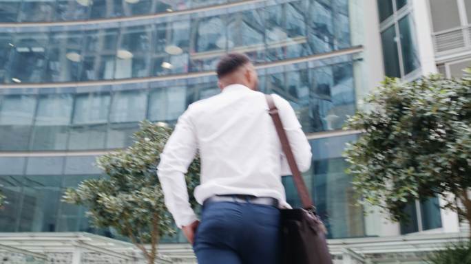 年轻商人独自在城市中行走的后视图。上班或下班时，公司专业人员会随身携带行李。低角度的男性主管环顾商业