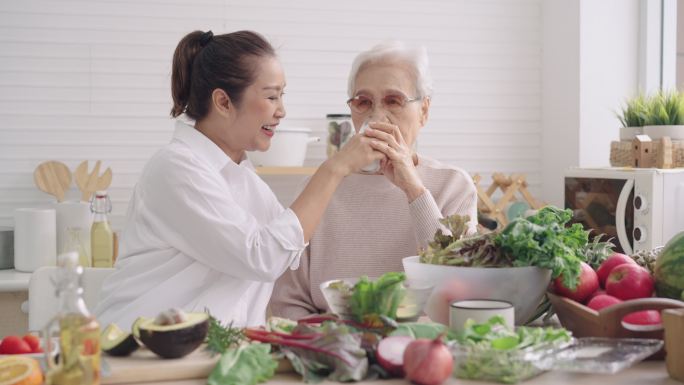 在厨房里用亚洲高级妈妈的牛奶喝健康饮料，与高级女儿一起准备早餐、蔬菜和水果，享受周末活动