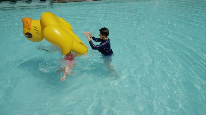 快乐的亚洲儿童在酒店或度假胜地与家人一起度假时，在泳池里玩黄鸭橡皮筏，生活方式理念。