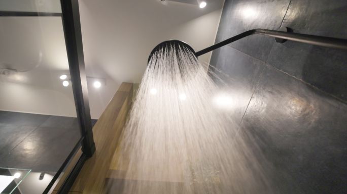 水从深蓝色现代豪华浴室的淋浴喷头流出。