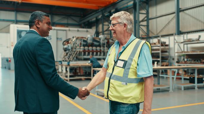 两名男子在工业设施握手。工程经理欢迎商人或投资者走过工厂。柴油机技工和老板在车间检查