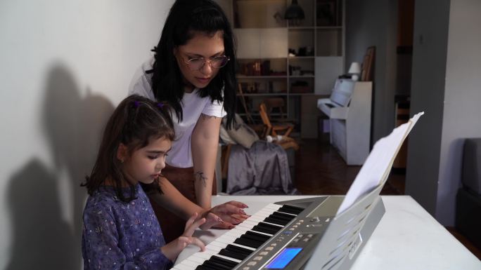 音乐家庭课。可爱的小女孩学习弹奏钢琴键盘合成器-在家学习音乐