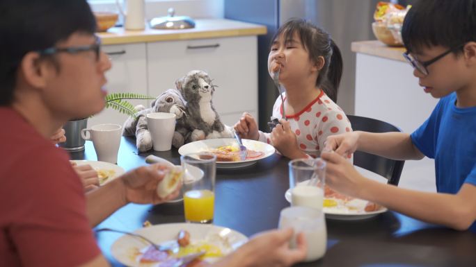 可爱的亚洲中国女孩与父母在厨房吃西式早餐