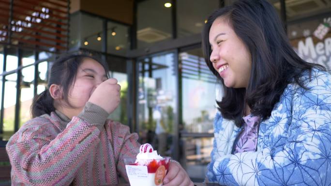 可爱的女孩在店外给妈妈喂香草冰淇淋