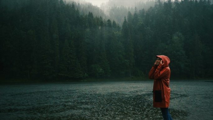 雨中，穿着雨衣的女子站在湖边