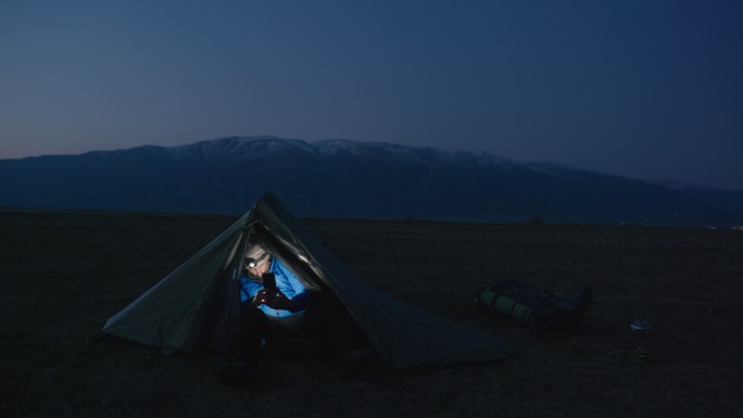 成熟的游客晚上在帐篷里打电话。在大自然中独自在山上露营。