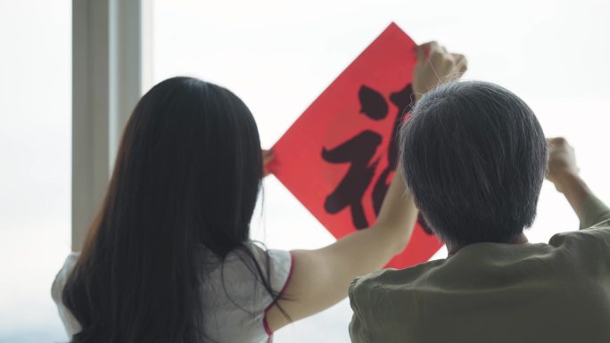 中国新年老人和女儿在窗户上用汉字书法装饰房子客厅，为家庭团聚做准备