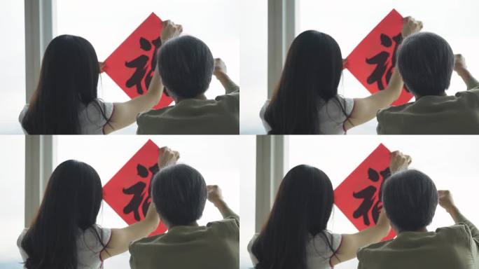 中国新年老人和女儿在窗户上用汉字书法装饰房子客厅，为家庭团聚做准备
