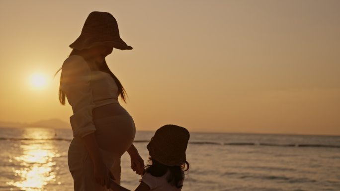 日落时分，女儿在海滩亲吻怀孕母亲的腹部轮廓